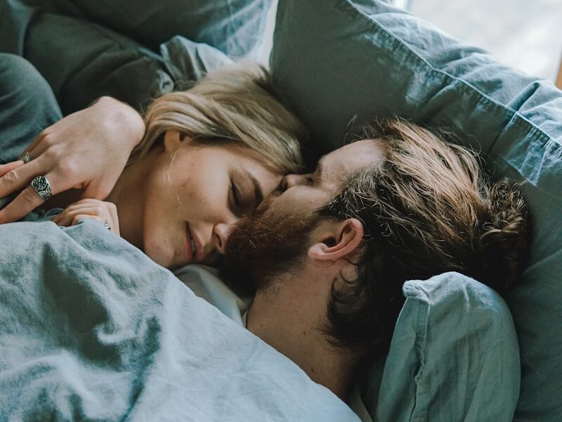 man kissing woman's forehead while lying on bed