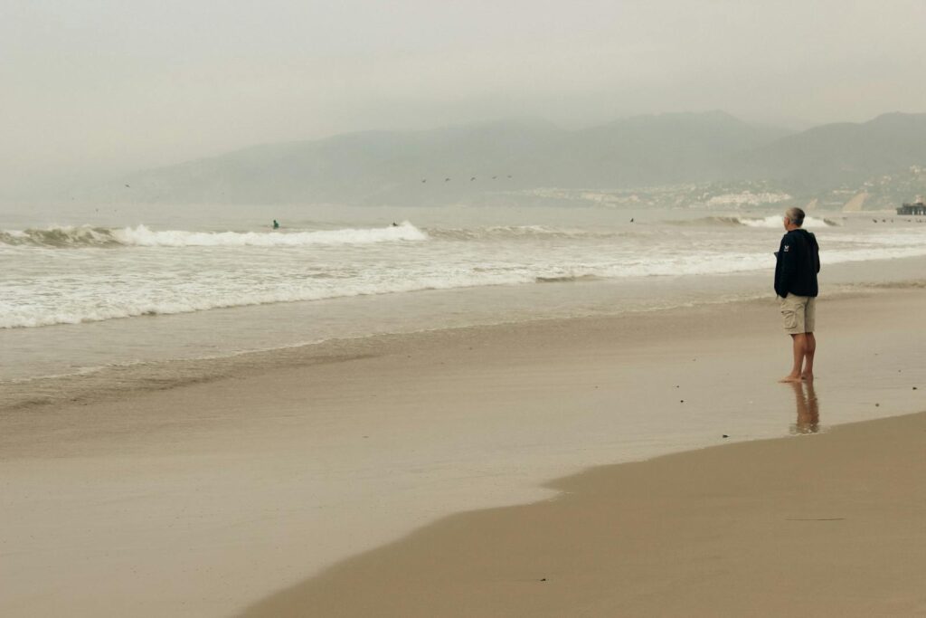 Elderly man walking along a misty beach, reflecting solitude and calmness in nature.