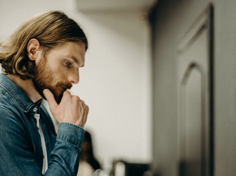 A man in deep thought while operating a printer in an office setting.