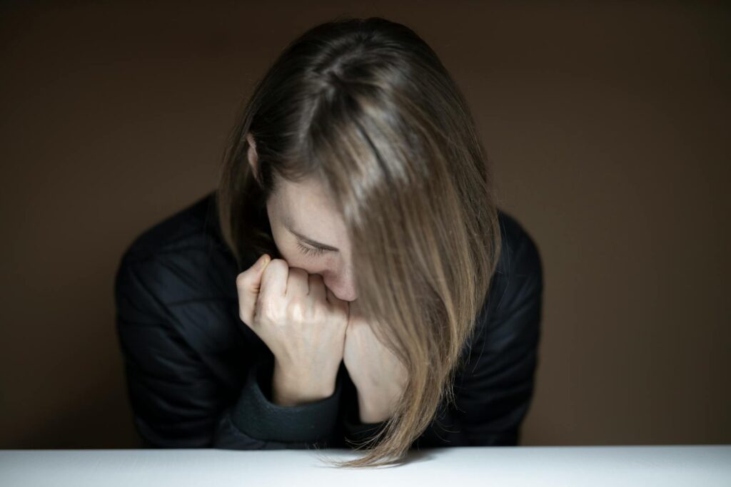 Young woman in a thoughtful pose with head down and crossed hands indoors.