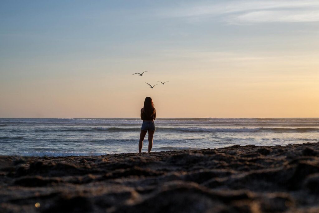 A woman enjoys a tranquil sunset on a Bali beach, capturing nature's beauty.