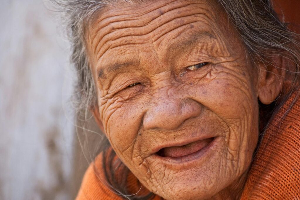 A heartwarming close-up portrait of a smiling elderly woman with deep wrinkles and joyful expression.