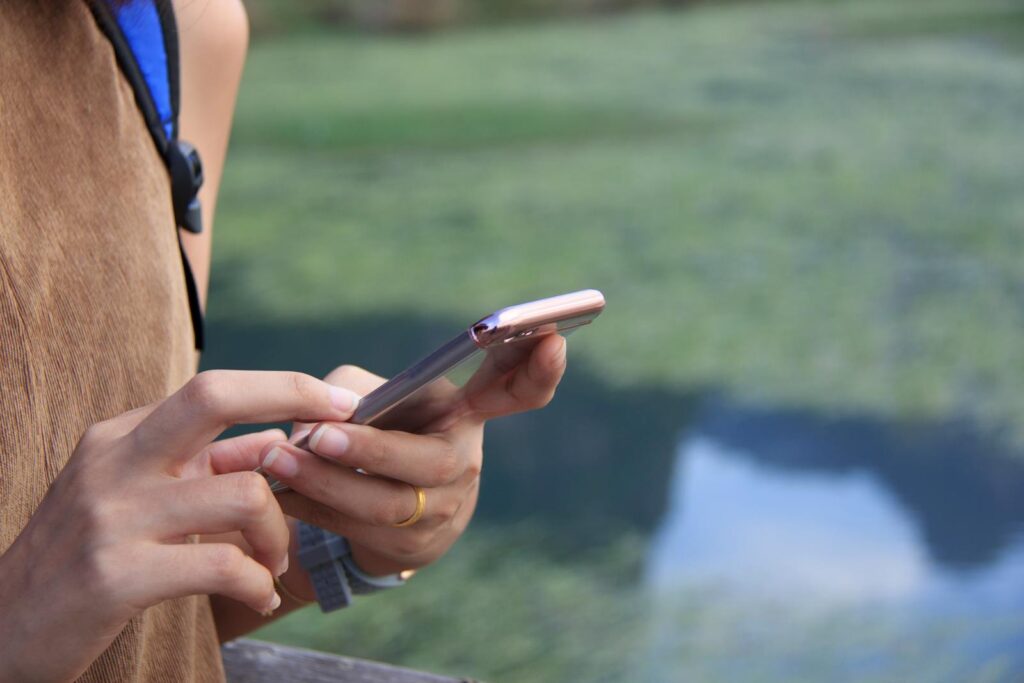 A young woman texting on her smartphone against a blurred natural background outdoors.