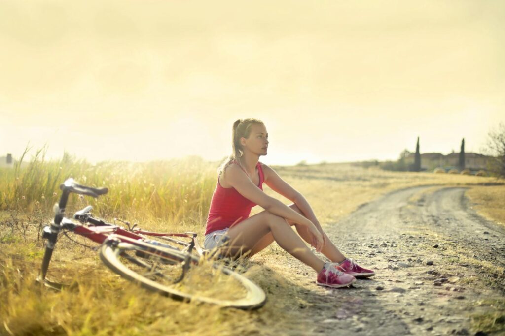 Woman sitting thoughtfully by her bicycle on a rural dirt road.