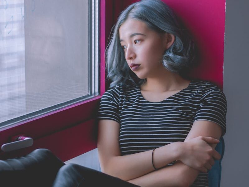 A woman sits by a window, deep in thought, conveying solitude.