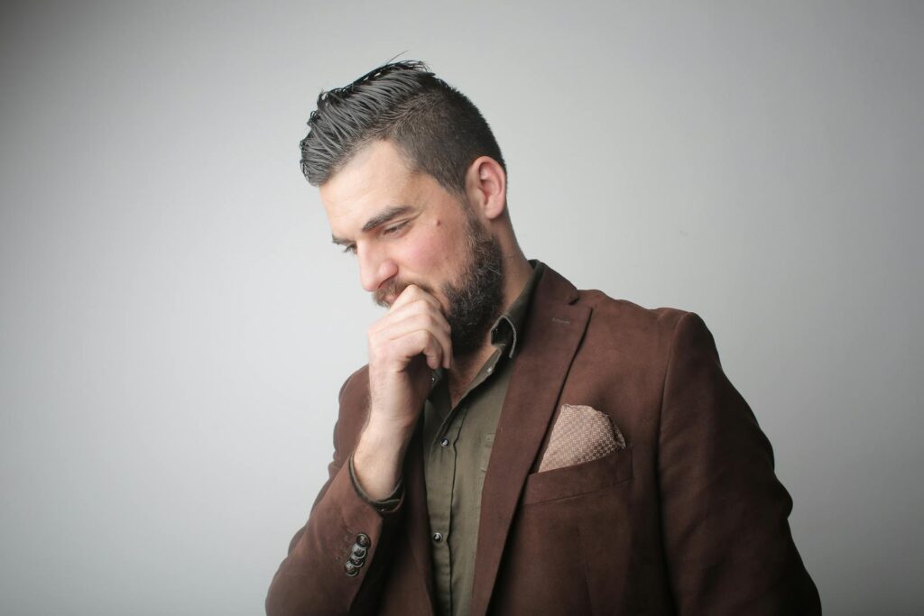 Thoughtful bearded man in brown suit contemplating in studio setting.