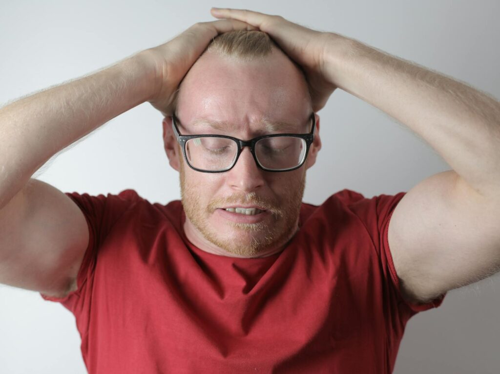 A man in a red t-shirt holding his head, showing expressions of stress and frustration.