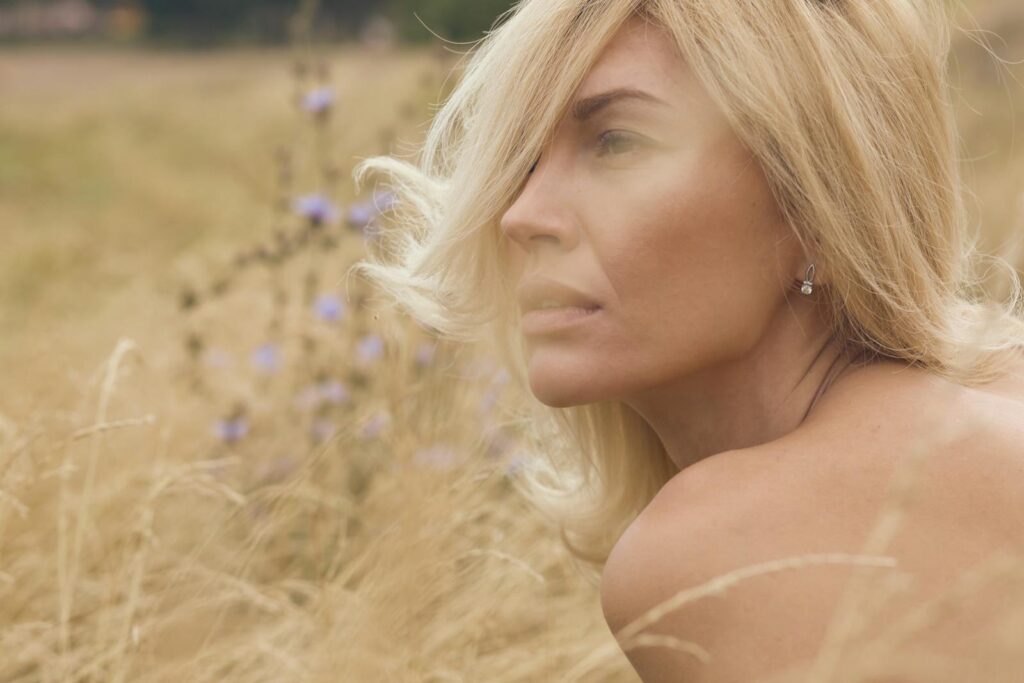 Close-up portrait of a blonde woman in summer field with pensive expression.