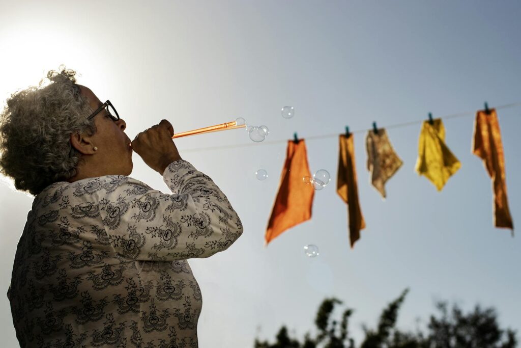 A joyful senior woman blowing bubbles under a clear sky with cloths on a line.