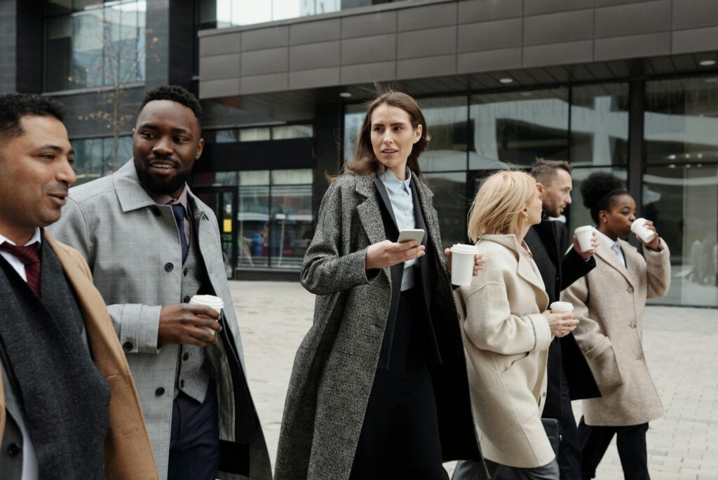 A diverse group of business professionals walking outside a modern building, enjoying coffee and conversation.