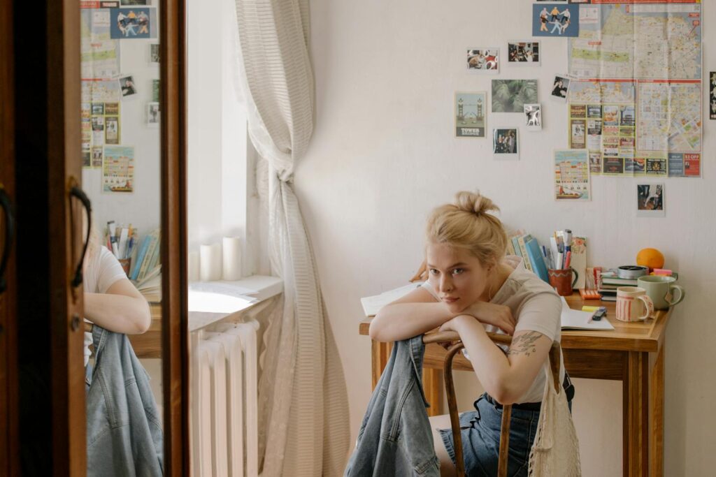 Young woman sitting at a desk reflecting, surrounded by personal items in a cozy dorm room.