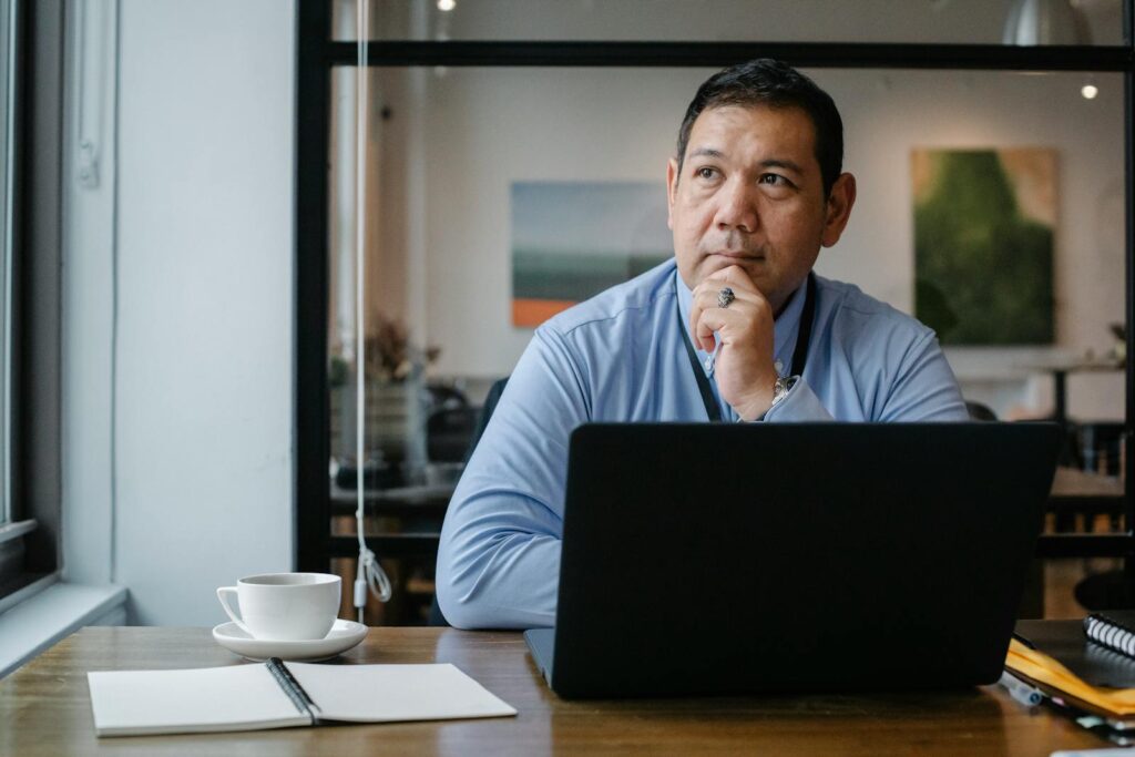 A businessman deep in thought while working on a laptop in a modern office setting.
