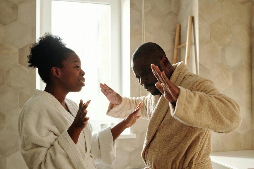 A couple in bathrobes having an emotional discussion in an indoor setting with expressive hand gestures.
