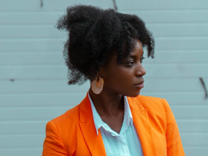woman wearing orange blazer standing near white wall