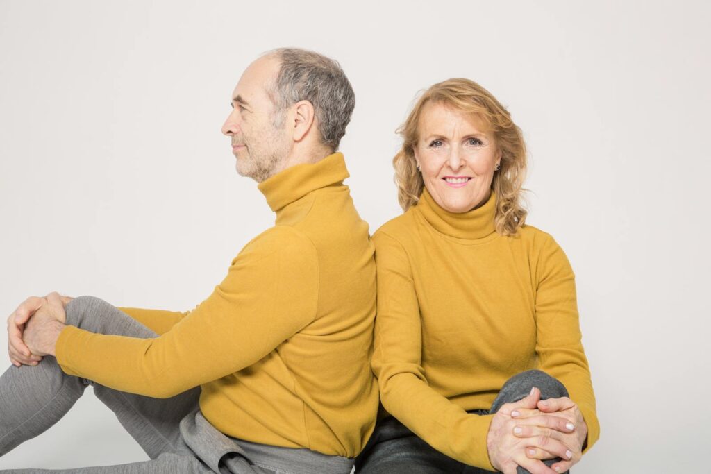 Happy senior couple sitting back to back in matching yellow sweaters, expressing love and togetherness.