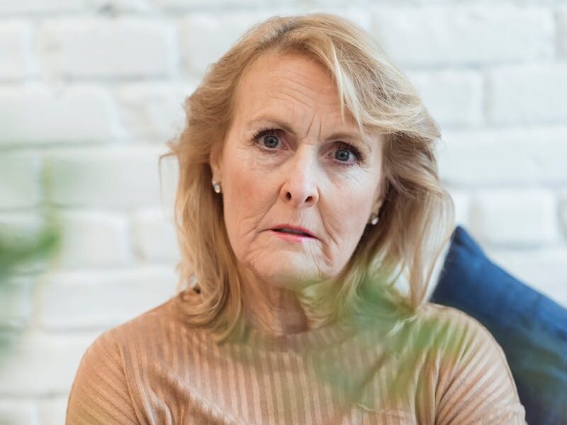 Serious elderly female in clothes with striped ornament looking at camera while sitting on sofa at home