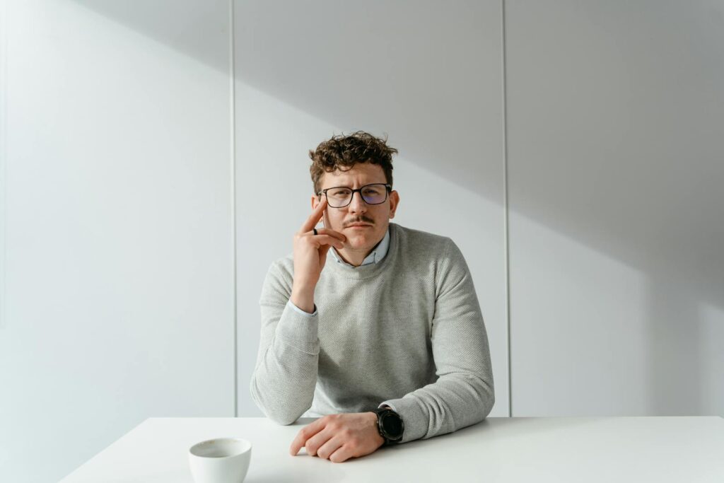 Man in glasses sitting at a bright and minimalist office desk, exuding a calm and focused demeanor.
