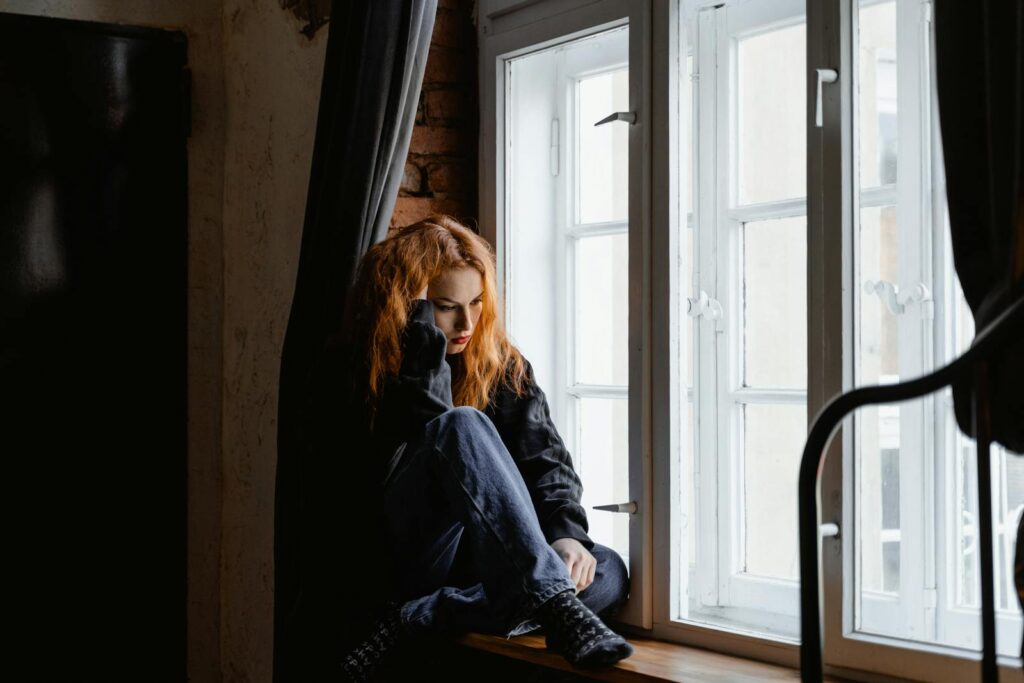 A woman sits by a window, lost in deep thoughts and moody light.