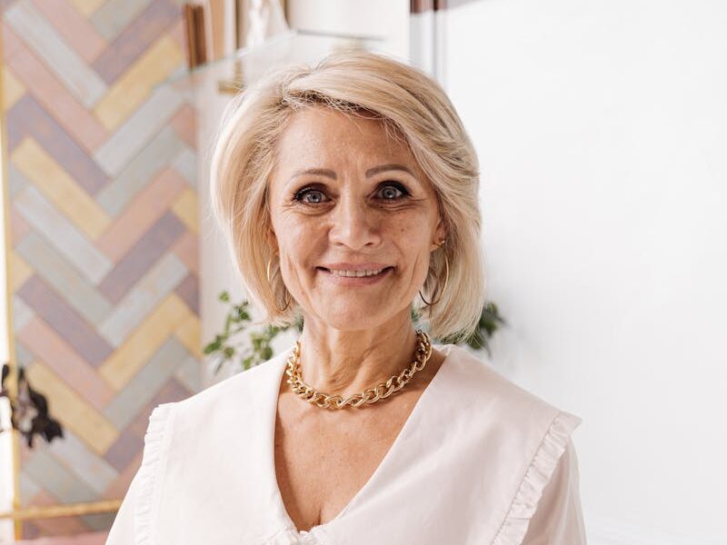 Smiling senior woman taking notes in a cozy, stylish room with pastel decor.