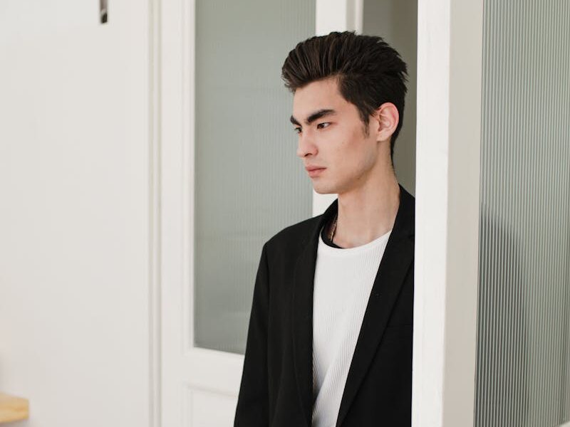 Asian man in formal attire standing at an open door, looking serious.
