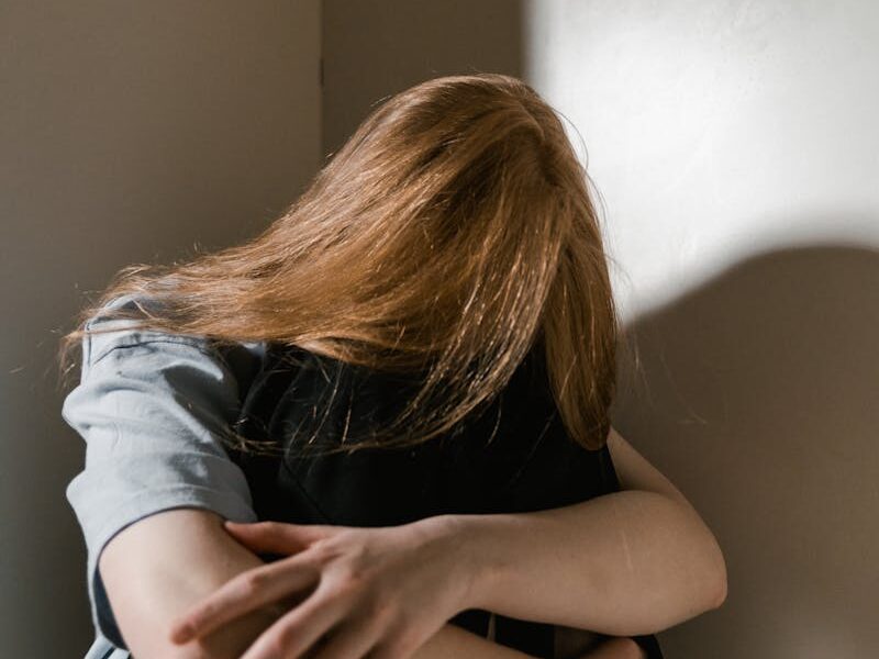 A woman sits alone in a corner, reflecting anxiety and solitude. Soft lighting accentuates her posture.