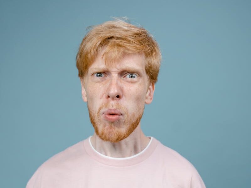 Adult man with angry facial expression in pink shirt, studio shot with blue background.