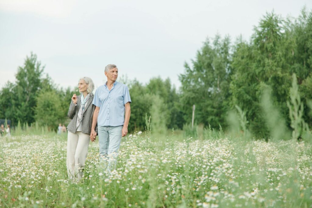 A senior couple enjoying a peaceful walk through a lush flower field on a sunny day.