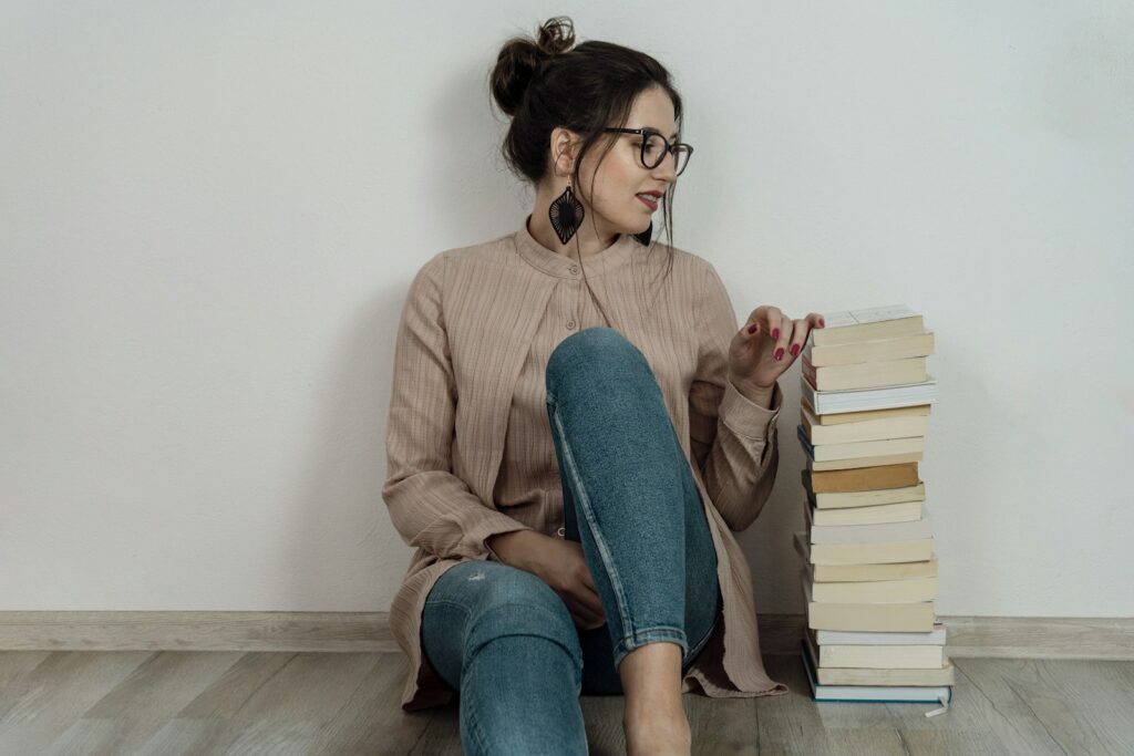 a woman sitting on the floor with a stack of books