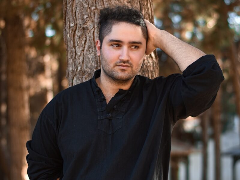 man in black polo shirt standing beside brown tree during daytime