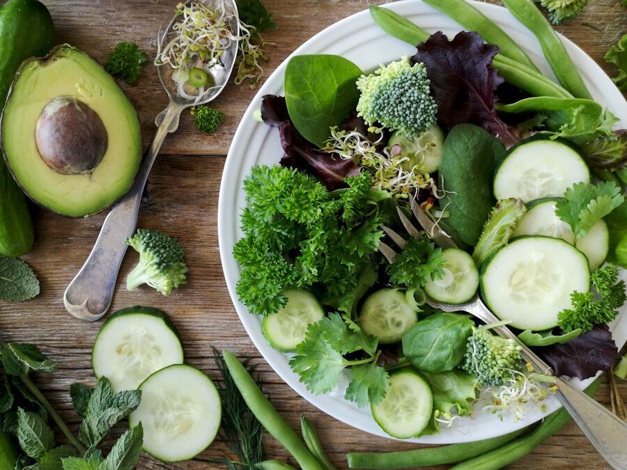 sliced broccoli and cucumber on plate with gray stainless steel fork near green bell pepper, snowpea, and avocado fruit