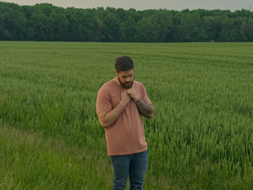 man in brown long sleeve shirt and blue denim jeans standing on green grass field during