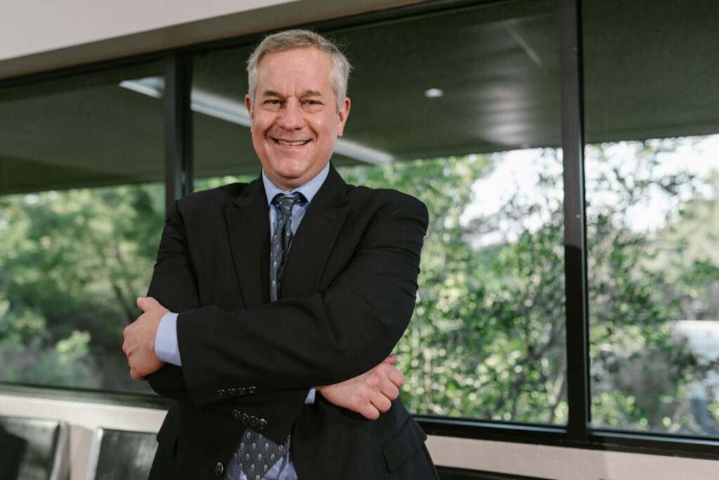 Smiling senior businessman with arms crossed standing confidently indoors.