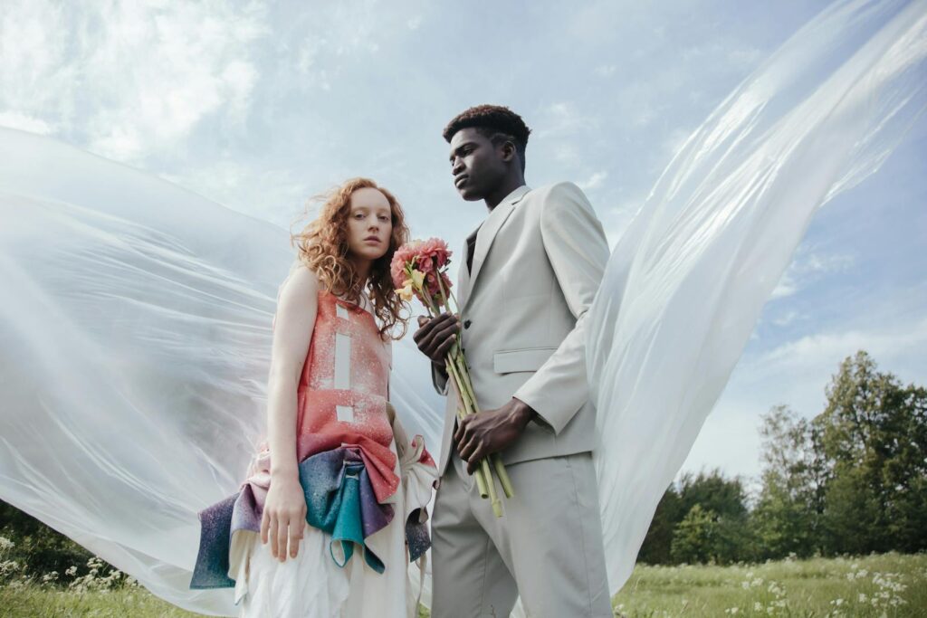 Fashionable young couple posing outdoors with flowers and flowing fabric.