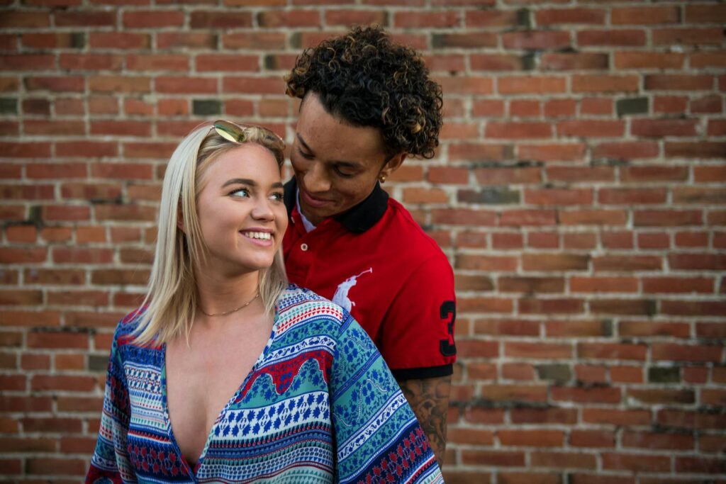 A loving couple sharing a joyful moment outdoors against a brick wall.