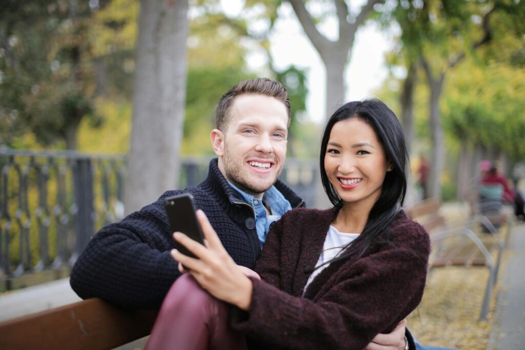Smiling couple sitting on a bench in a park, capturing a joyful moment together.