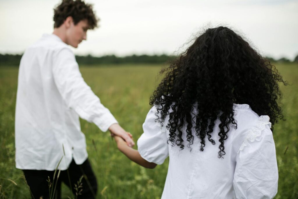 Couple walking hand in hand through a lush summer meadow, showcasing love and connection.
