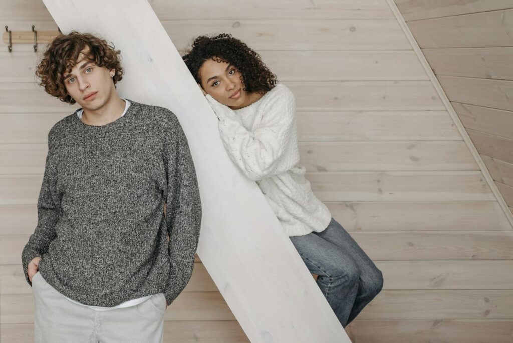 Young diverse couple posing casually indoors in warm sweaters, exuding a relaxed and cozy atmosphere.