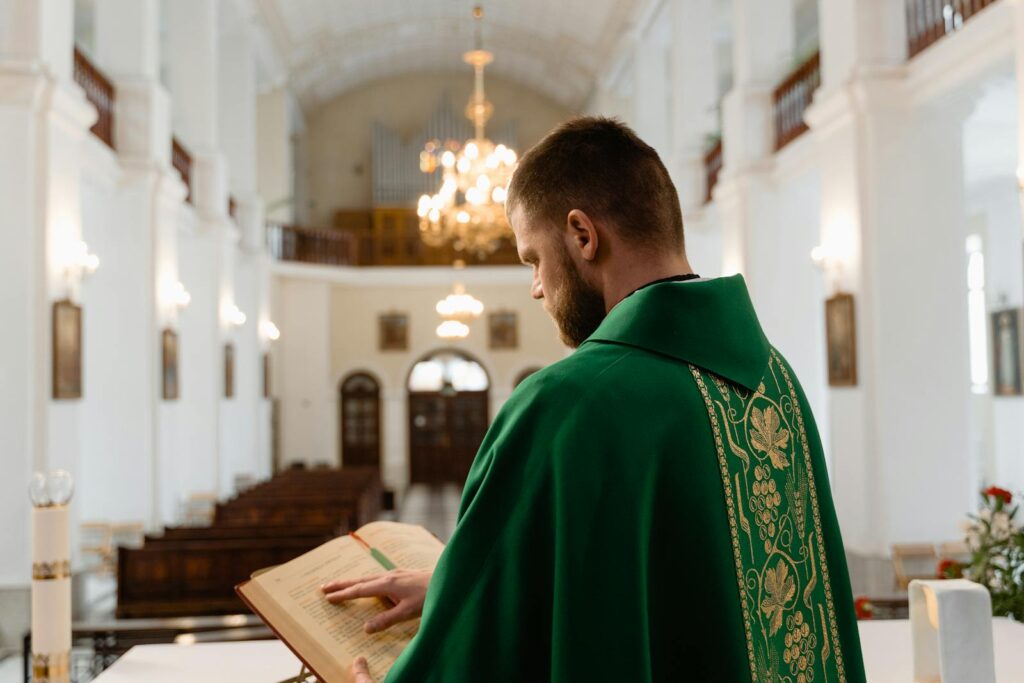 A priest in green vestment reading during a religious service in a grand cathedral.