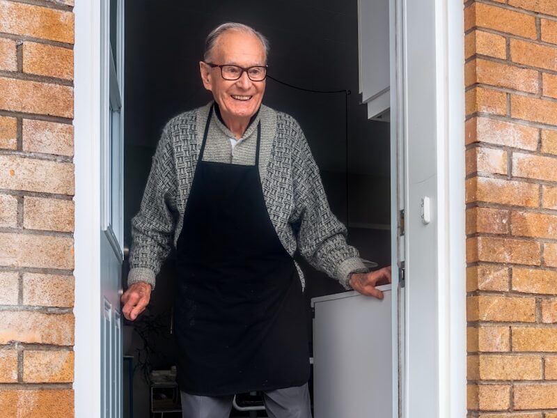 man in black vest and black dress pants standing beside white wooden door