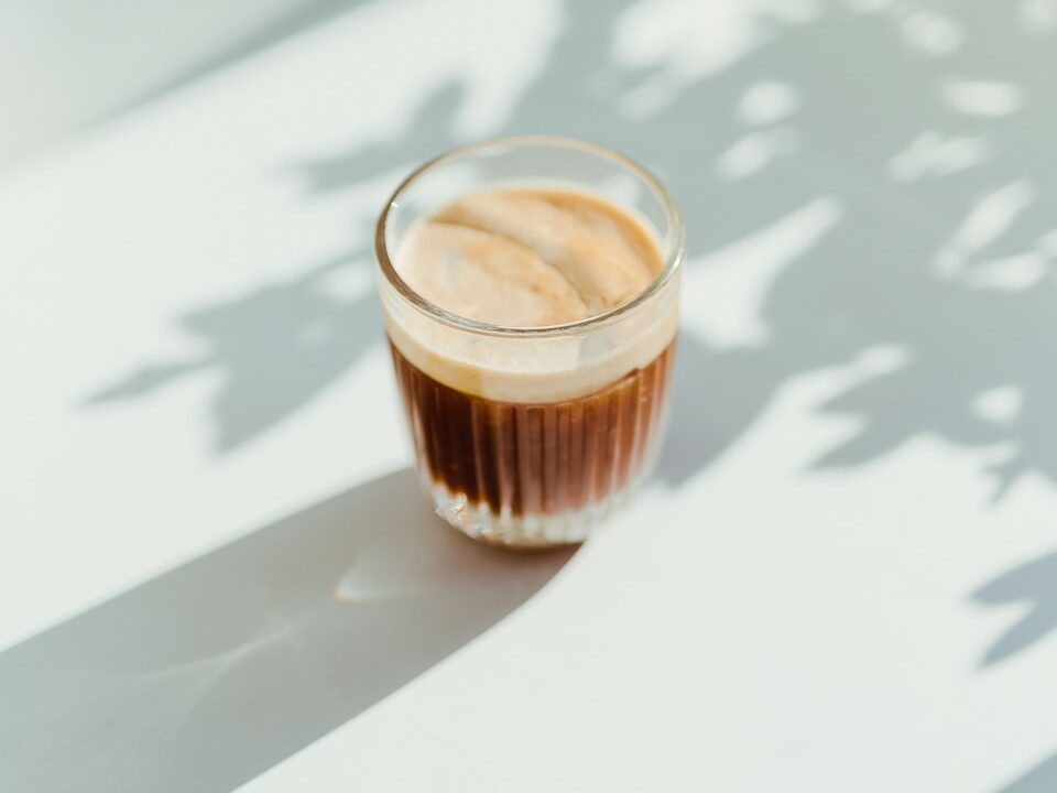 clear drinking glass with coffee on top of white table